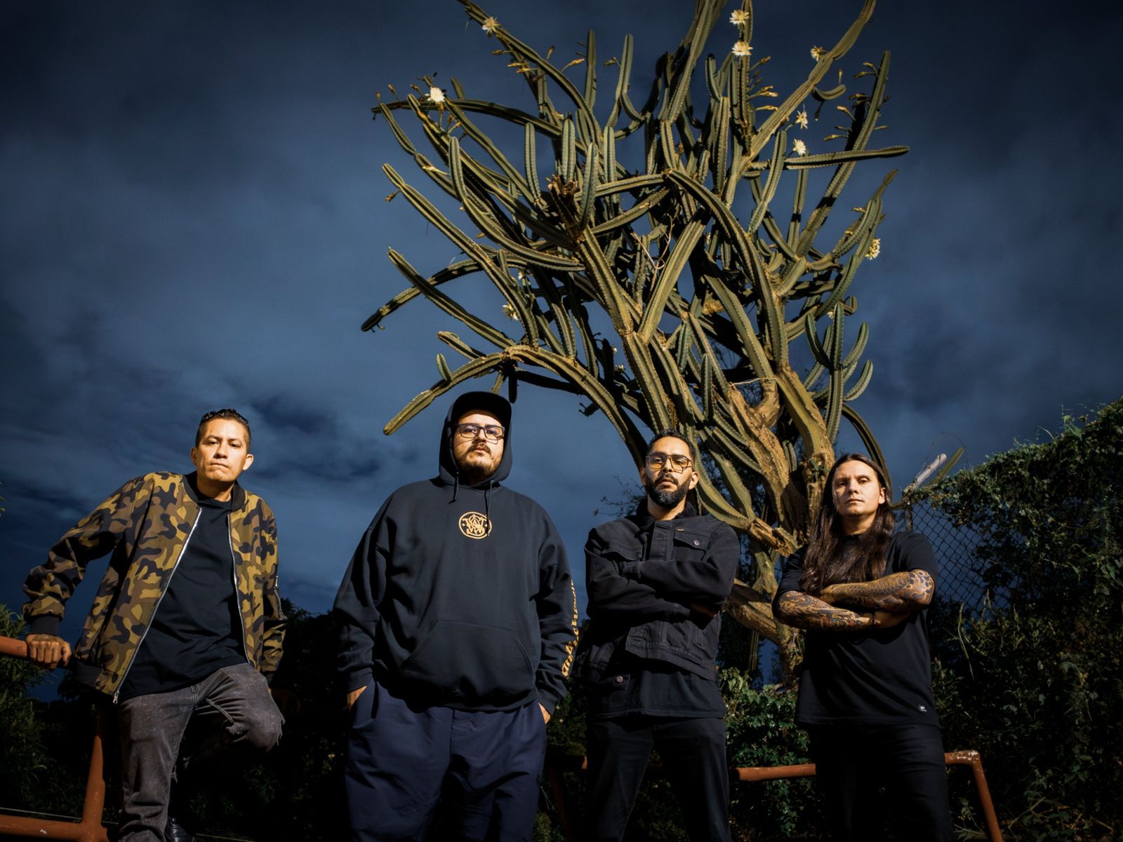 La banda de noche frente a un cactus gigante bajo un cielo azul