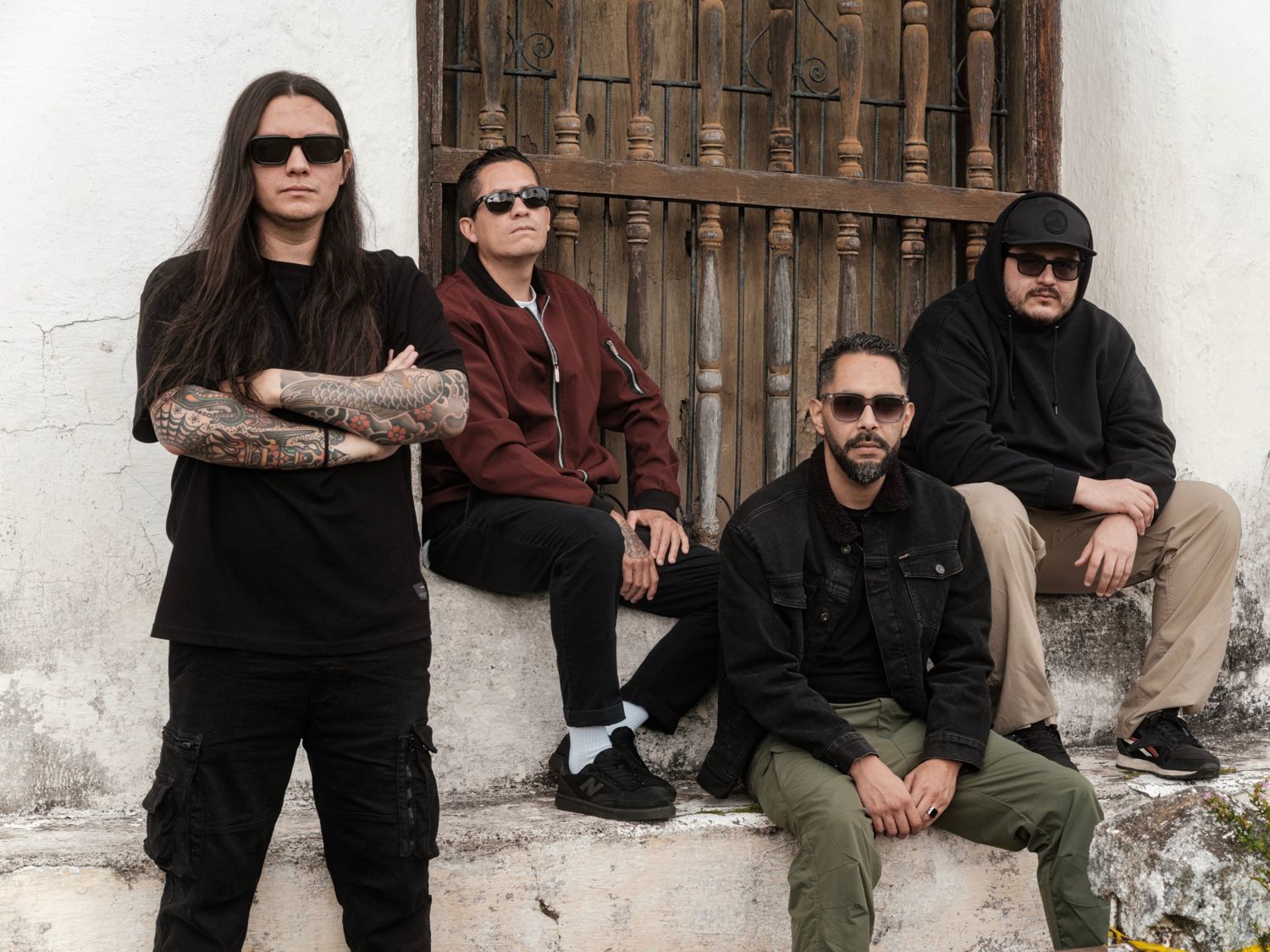 La banda junto a una ventana de balaustres, Gustavo de pie con los brazos cruzados